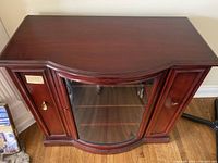 Front view showing curved glass door flanked by wood panel doors with metal handles, polished wood finish.