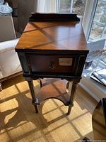 Front view of the side table showing the drawer and knob, with sunlight casting shadows from window.