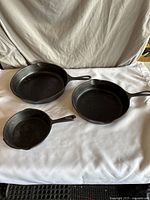 Three cast iron pans laid on a white cloth background showing all three sizes together.
