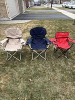 Three folding chairs on grass: beige, blue (same type), and red (different type)