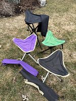 Four camping stools arranged on grass, showing two black stools, one purple, and one green stool, with one purple foldable carrying case on the ground