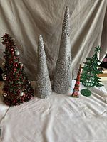 Five Christmas-themed trees displayed on a white cloth background, showing size variations and different materials and styles