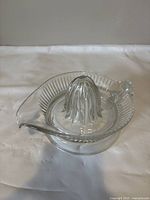 Front-left angle of the clear glass hand juicer showing ribbed reamer and pouring lip