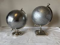 Two silver globes showing different bases and similar size.