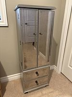 Front view of tall standing mirrored jewelry cabinet with closed doors and two bottom drawers