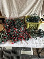 Wide view of large lot of assorted Christmas lights piled on tabletop, with some strands in a yellow plastic basket.