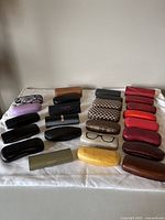 Full view of 26 assorted glasses and sunglasses cases in various sizes, colors, and patterns laid out on a white surface.