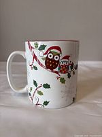 Front view of the large white ceramic mug featuring two owls in Santa hats sitting on a holly branch with candy canes and holly leaves design.