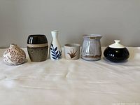 Front view of all six unique vases side by side on a white surface