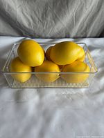 Photo of six bright yellow decorative lemons in a clear rectangular plastic container.