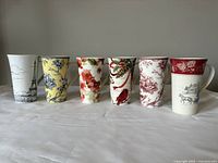 Photo showing all six tall mugs in a row, each with a different decorative design.