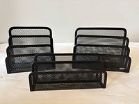 Front view of three black metal mesh paper organizers of different sizes showing multiple slots for paper sorting.