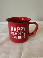 Front angled view of the red camping mug with white text and black rim and handle edge.