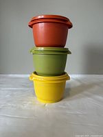 Three vintage Tupperware bowls stacked, showing orange, green, and yellow colors with lids on.