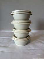 Four white vintage Tupperware bowls stacked vertically showing smooth exterior and lids fitting tightly on each bowl.
