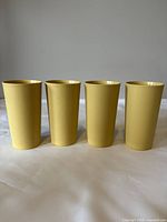 Four yellow vintage Tupperware drinking cups arranged in a row showing front.