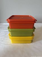 Stacked view of three vintage Tupperware square containers in orange, green, and yellow with lids.