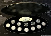 Original black elongated presentation box open showing 12 encapsulated proof coins arranged in two rows with a central plaque identifying the set.