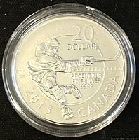 Obverse side of silver coin featuring hockey player in mid-shot with inscriptions indicating denomination, year, country, and silver purity.