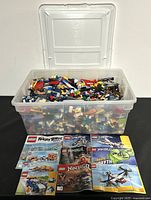 Clear plastic container filled to the top with assorted LEGO bricks in various colors and shapes, seen from the front with the open lid.