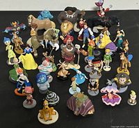 Overview photo showing over 30 assorted Disney character figurines including many well-known characters such as Simba, Pocahontas, Ariel, Belle, and more.