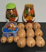 Two large Mr. Potato Head shaped clear containers filled with assorted accessories and orange plastic potato bodies in front along with a small container of parts on a black surface.