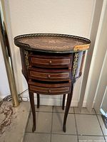 Full front-left view of oval side table showing three drawers, bronze gallery rail and cabriole legs