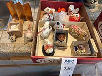 Photo of ceramic figurines including zodiac animals, small cloth dog, and a red Daruma doll arranged in a box and on a counter surface.