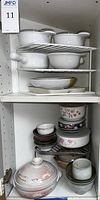 White ceramic bowls with handles and glass lids on top shelf, various ceramic bowls and dishes on lower shelves in cabinet.