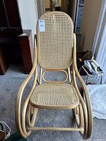 Front view of natural bentwood rocking chair with rattan seat and backrest and auction tag visible.