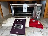 Photo of the Breville toaster oven, two pairs of oven mitts (one white, one red), and the instruction manual placed in front.