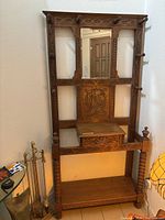 Full view of the carved wooden hall tree showing mirror, hooks, and base shelf.