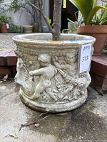 Photo of large stone/ceramic planter with raised cherub relief decoration and JMPO auction label attached.