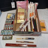 Wide view of assorted chopsticks including boxed, loose, plastic, wooden, disposable, and ceramic rests all arranged in a box and around it