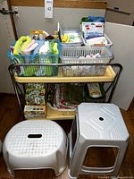 Full lot view showing two plastic step stools in front, baskets on table containing wash cloths, brushes, gloves and towels, boxes of BioBag food scrap bags underneath.
