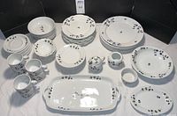 Full set arranged on table with all pieces visible including plates, bowls, mugs, serving platters, creamer, and medium dishes