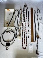 Full view of jewelry assortment including bolo tie, necklaces, chains, earrings, and sterling silver pieces in a box with a ruler for scale