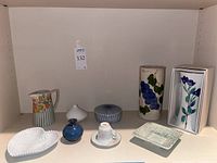 Shelf display of various decorative porcelain and ceramic items including vases, teacup, and small dishes.