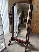 Front view of freestanding full length mirror showing cherry wood frame and stand with curved legs.