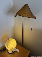 Both items in the room corner: the small illuminated globe on a low wooden table and the tall floor lamp next to the wall with amber beaded shade.