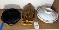 Three items on shelf: black cast iron pot with lid, brown-yellow ceramic fish-shaped serving dish, white ceramic hot pot with lid