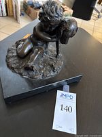 Front view of sculpture on black stone plinth with auction tag visible