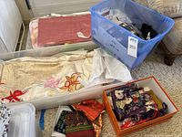Wide view showing assorted kimonos in fabric and partially completed states and multiple scarves in orange box along with a storage bin with more textiles.
