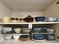 Shelves with various ceramic and stoneware serving bowls, crocks with lids, and bowls in multiple colors and designs.