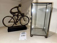 Metal sculpture of a person riding bike on black base next to glass display case