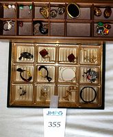 Wooden and plastic trays with assorted costume jewelry pieces laid out for inventory.