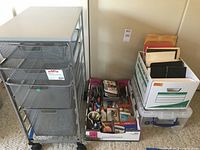 Grey Elfa metal rolling cart with 4 mesh drawers next to office supplies in trays and boxes