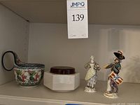 All four items displayed on shelf: ceramic cup, hexagonal container with lid, two figurines