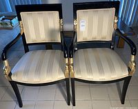 Front view of both chairs showing black lacquer frames, cream striped upholstery and gold-tone detailing