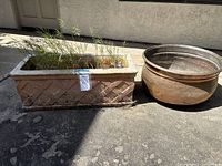Photo showing side view of the rectangular concrete planter with criss-cross pattern and the rounded Turkish copper pot side by side outdoors on pavement, planter with grass inside.